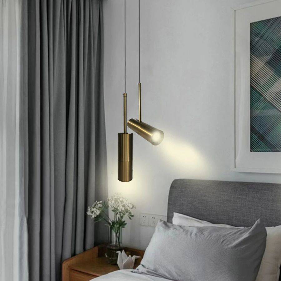 Clérachic two brass cylinder pendants beside a grey-upholstered bed, one head angled to wash light onto the wall.