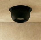 Clérachic matt black spherical downlight tilted in its round trim, set into a plaster ceiling above a textured wall.