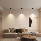 Clérachic row of three black adjustable downlights washing a cream wall with soft pools of light above a modular sofa.