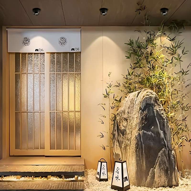 Clérachic three black downlights above a glazed entrance with bamboo and a rock, casting warm pools down the wall.