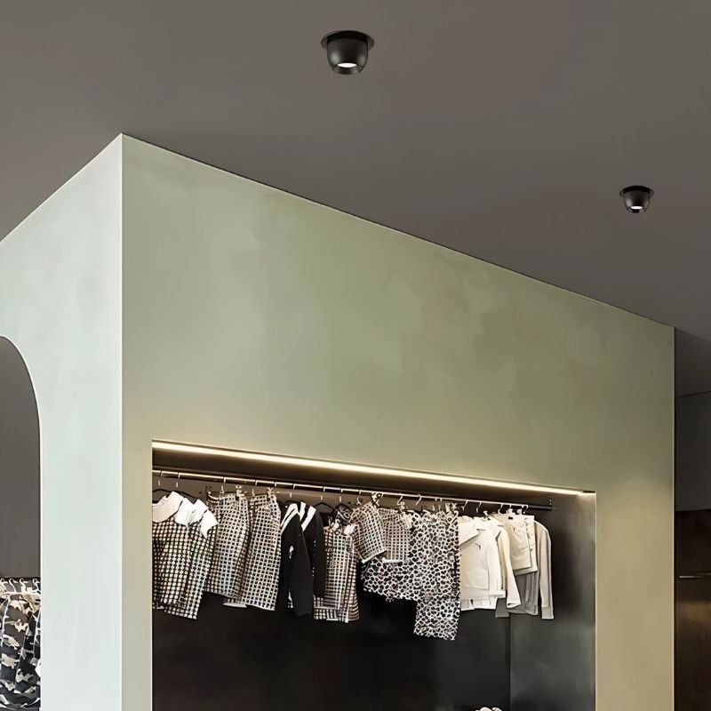 Clérachic two black adjustable downlights set into a dark ceiling above a boutique clothes rail with a strip light.