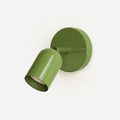 Green Clérachic wall light with a round backplate and a tilting cylindrical head, angled down on a plain white backdrop.
