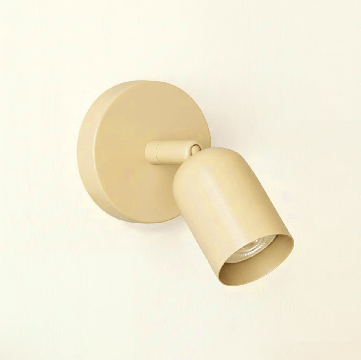 Soft cream-beige Clérachic wall light with a round plate and a short tilting head, seen against a warm cream wall.