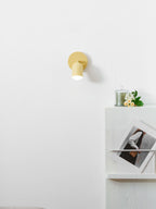 Lit yellow Clérachic wall light above a white cabinet with a candle, a bunch of flowers and a framed print leaning on it.