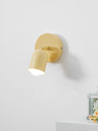 Close view of a butter-yellow Clérachic wall light, its tilted head glowing, above a white ledge with flowers under glass.