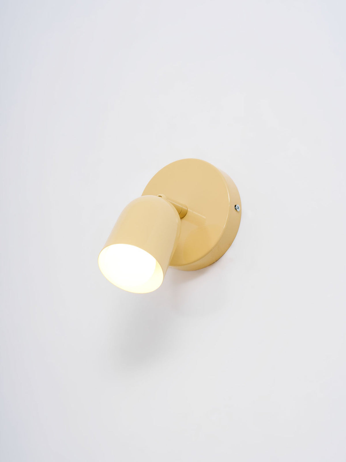 Lit Clérachic wall light in butter yellow, its head pointed down and left, on a pale grey-lilac wall.