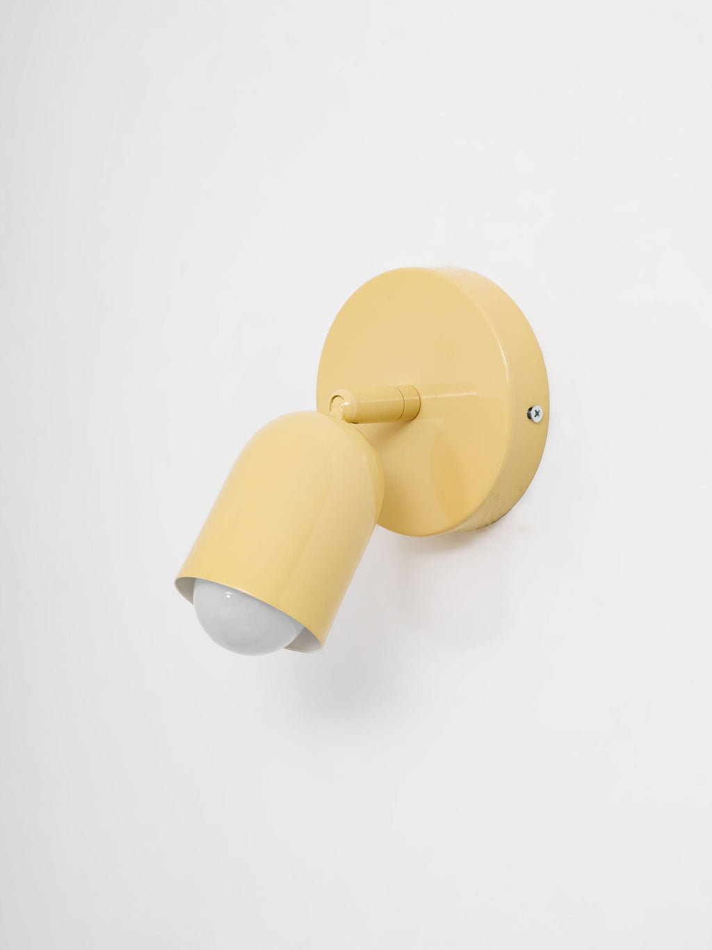 A yellow Clérachic wall light turned toward the left, the bulb showing in its head, against a pale grey wall.