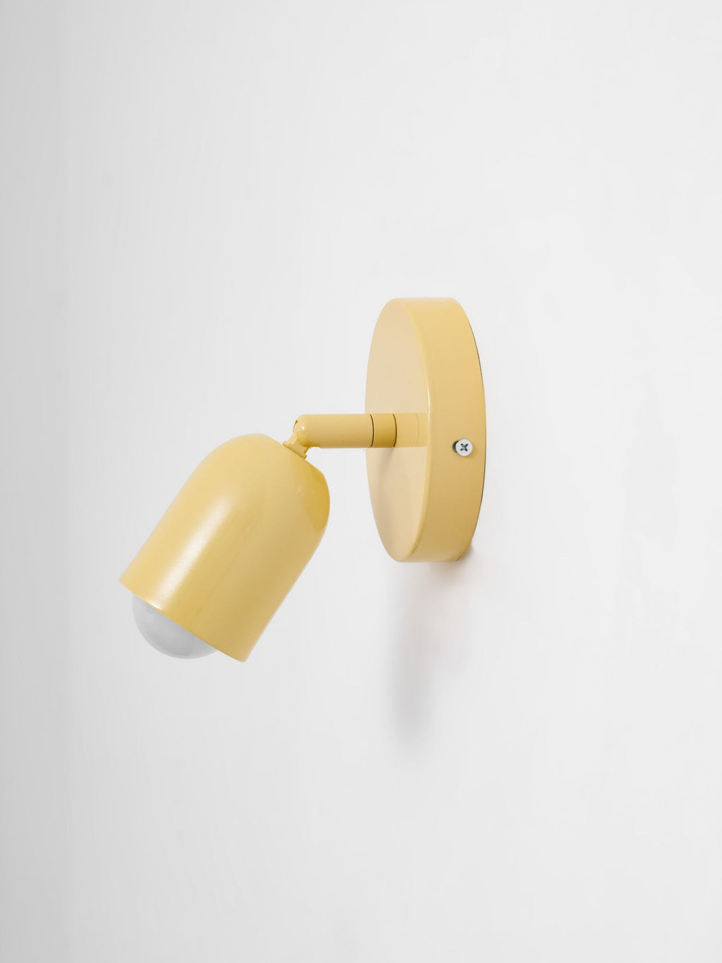 Side view of a yellow Clérachic wall light with the head angled down and the round bulb just visible, on pale grey.