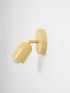 Side view of a yellow Clérachic wall light with the head angled down and the round bulb just visible, on pale grey.