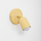 Close-up of a butter-yellow Clérachic wall light, its round backplate with a small screw and a bulb in the angled head.
