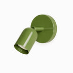 Green Clérachic wall light with a round backplate, its cylindrical head tilted forward and the bulb visible inside, on white.