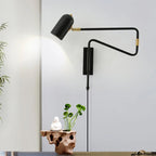 Clérachic adjustable wall light in black with a gold collar, lit above a rust-coloured sculptural stand holding a white figurine and a small green plant.