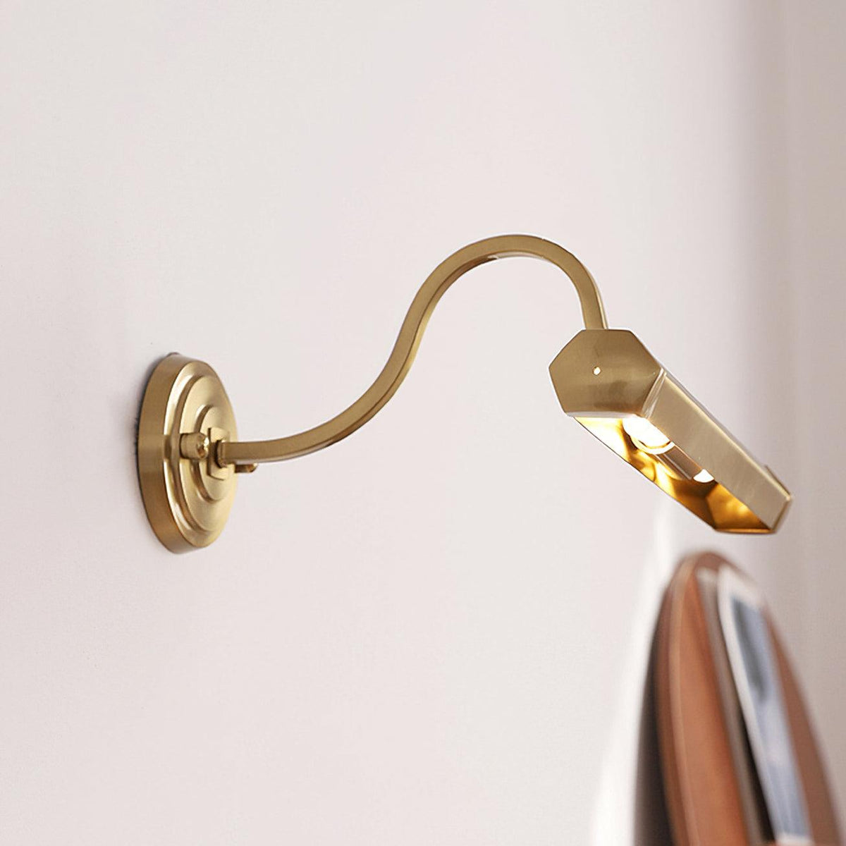 Tilted down on its long S-shaped arm, this gold Clérachic wall light shows the polished inside of its hexagonal shade.