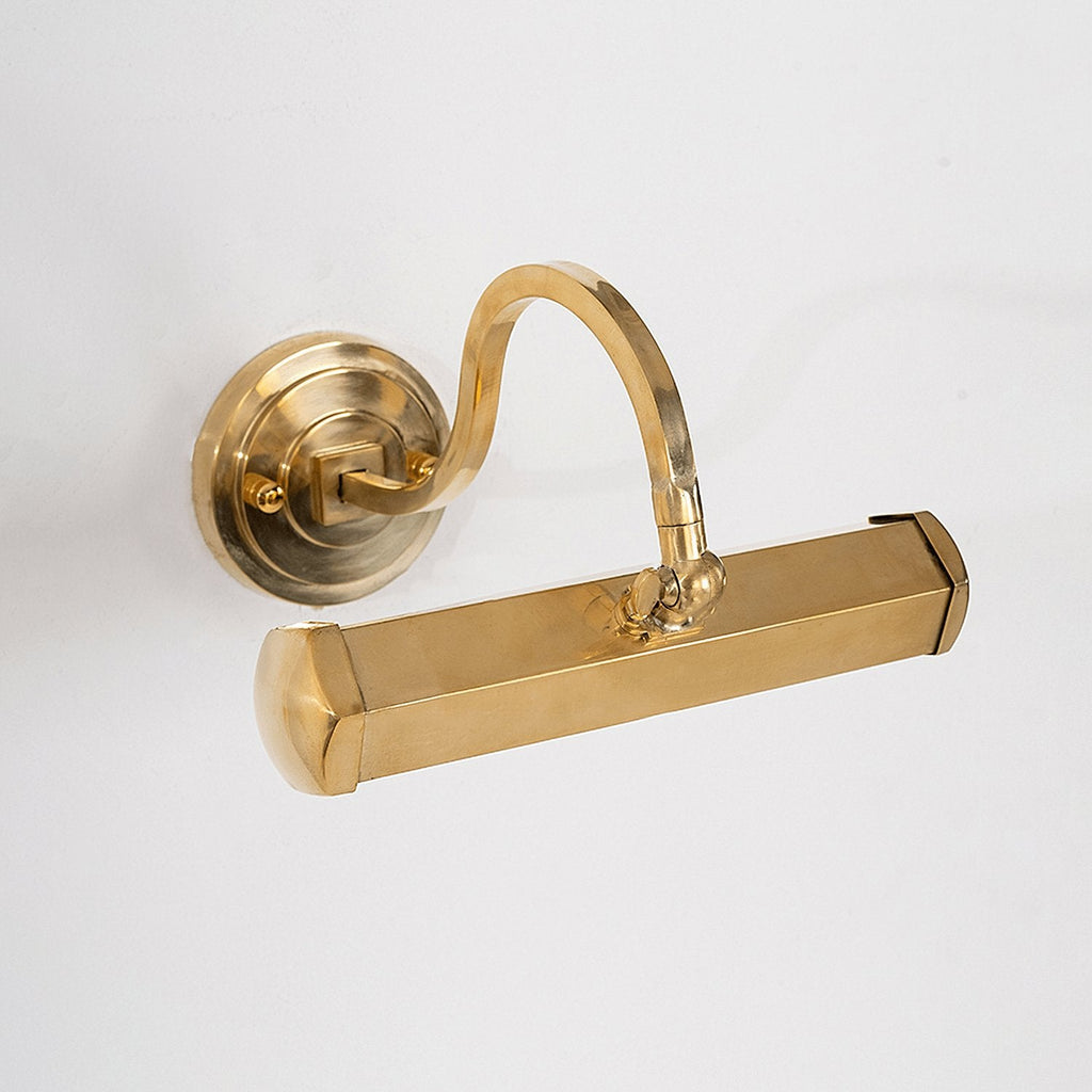 Angled close-up of the gold bar shade and the pivot joint on this Clérachic wall light, with its round backplate at the left.