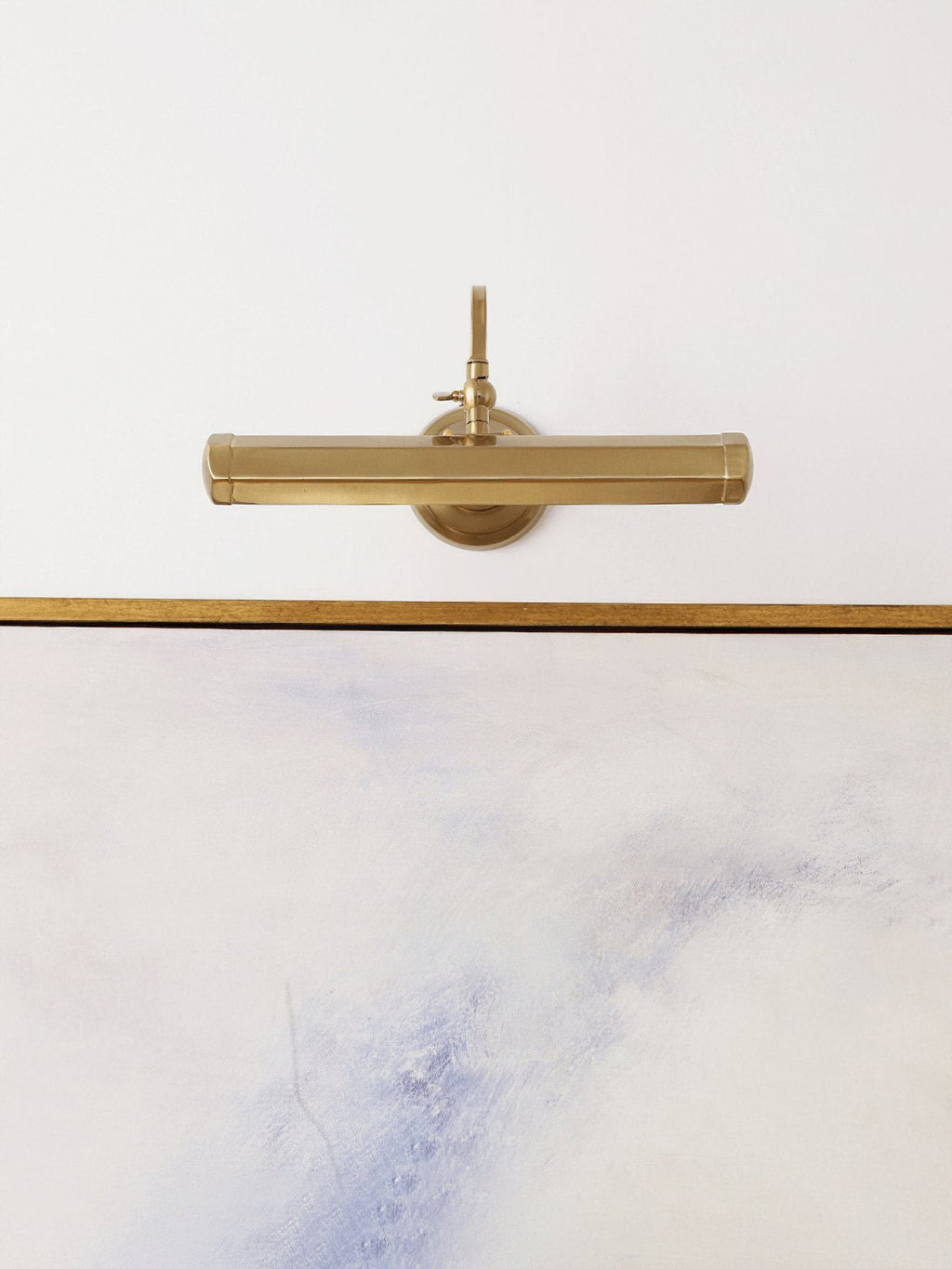 Straight-on view of the gold bar shade of this Clérachic wall light, hung above the gold edge of a pale painting.