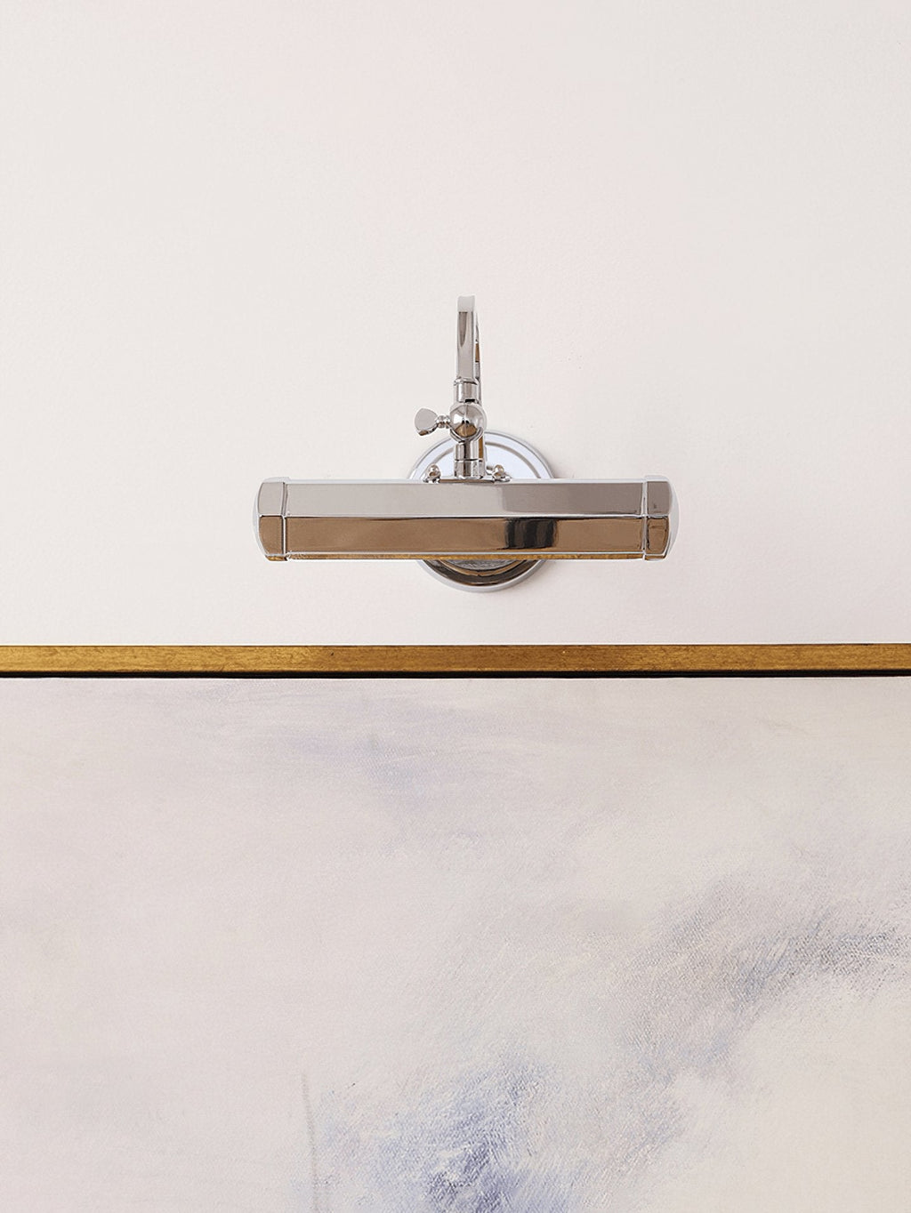 A chrome version of this Clérachic wall light, seen straight on above a gold-edged abstract canvas.