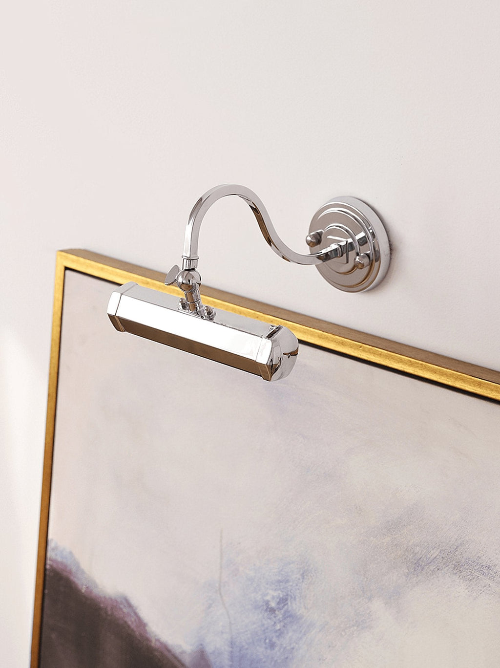 Chrome Clérachic wall light angled down over the corner of a gold-framed painting, with its swan-neck arm and round plate.