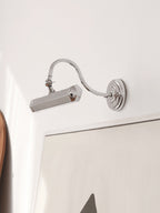 Chrome Clérachic wall light with a curved arm, tilted down beside a white frame, on a pale wall.