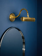 Gold Clérachic wall light on a deep blue wall above an arched mirror, with its curved arm reaching out to the shade.