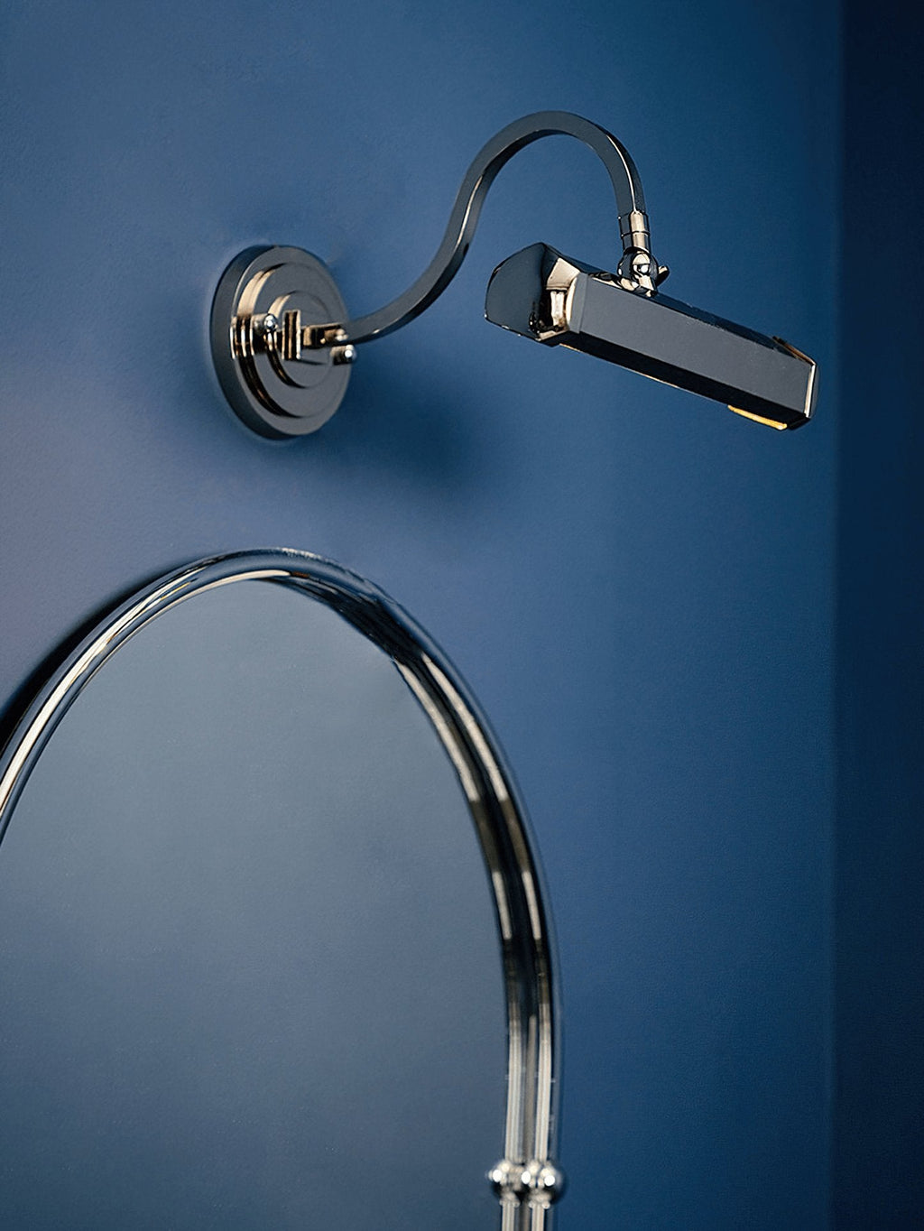 Against a deep blue wall and an arched chrome mirror, this chrome Clérachic wall light angles its shade out to the right.