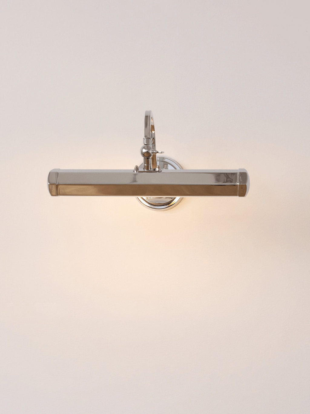 Chrome Clérachic wall light lit from within, throwing a warm glow across a peach-toned wall.