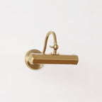 Gold Clérachic wall light with a hexagonal shade and short curved arm, shown straight on against a pale backdrop.