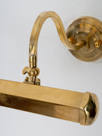 Close view of the gold arm, wing-screw pivot and rounded end cap of the shade on this Clérachic wall light.