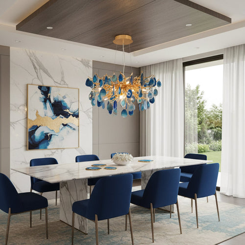 Blue agate Clérachic chandelier above a white marble dining table with navy chairs, with a seaside view through the glass doors.
