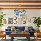 A blue agate Clérachic chandelier hanging in a living room with exposed ceiling beams, a navy sofa and rattan armchairs.