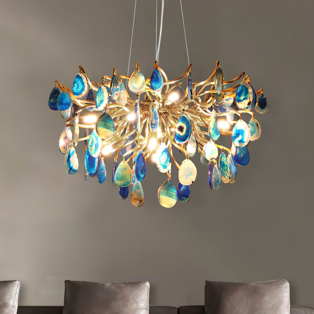 Lit Clérachic chandelier with blue and green agate slices on a branching gold frame, hanging against a grey wall above a sofa.