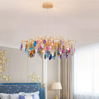 Clérachic chandelier with multicolour agate slices hanging over a bedroom with a blue patterned headboard and gold wall details.