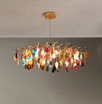 Lit Clérachic chandelier with multicolour agate slices, its gold branches glowing against a grey wall.