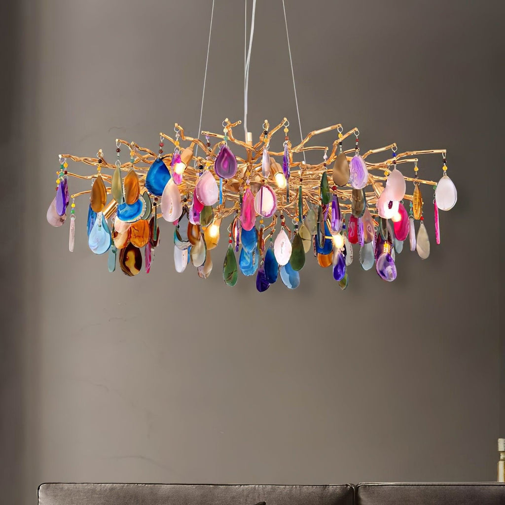 Clérachic chandelier with pink, purple, blue and orange agate slices hanging below a gold branch frame, in front of a grey wall.