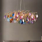 Clérachic chandelier with pink, purple, blue and orange agate slices hanging below a gold branch frame, in front of a grey wall.