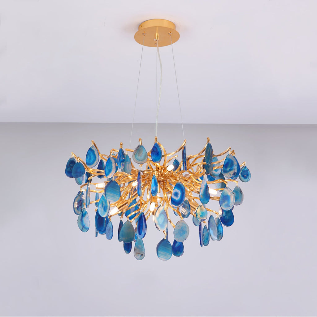Blue agate Clérachic chandelier on a pale grey backdrop, its teardrop slices hanging below a gold branch frame.