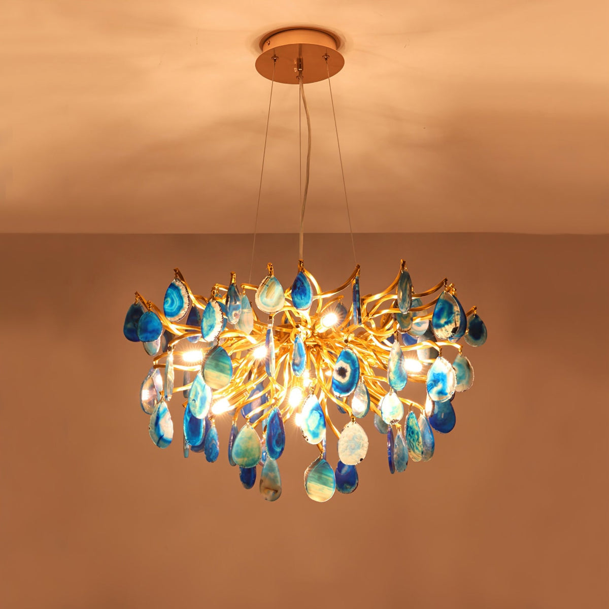 Lit blue agate Clérachic chandelier against a warm orange ceiling, light showing through the teal and blue stone slices.