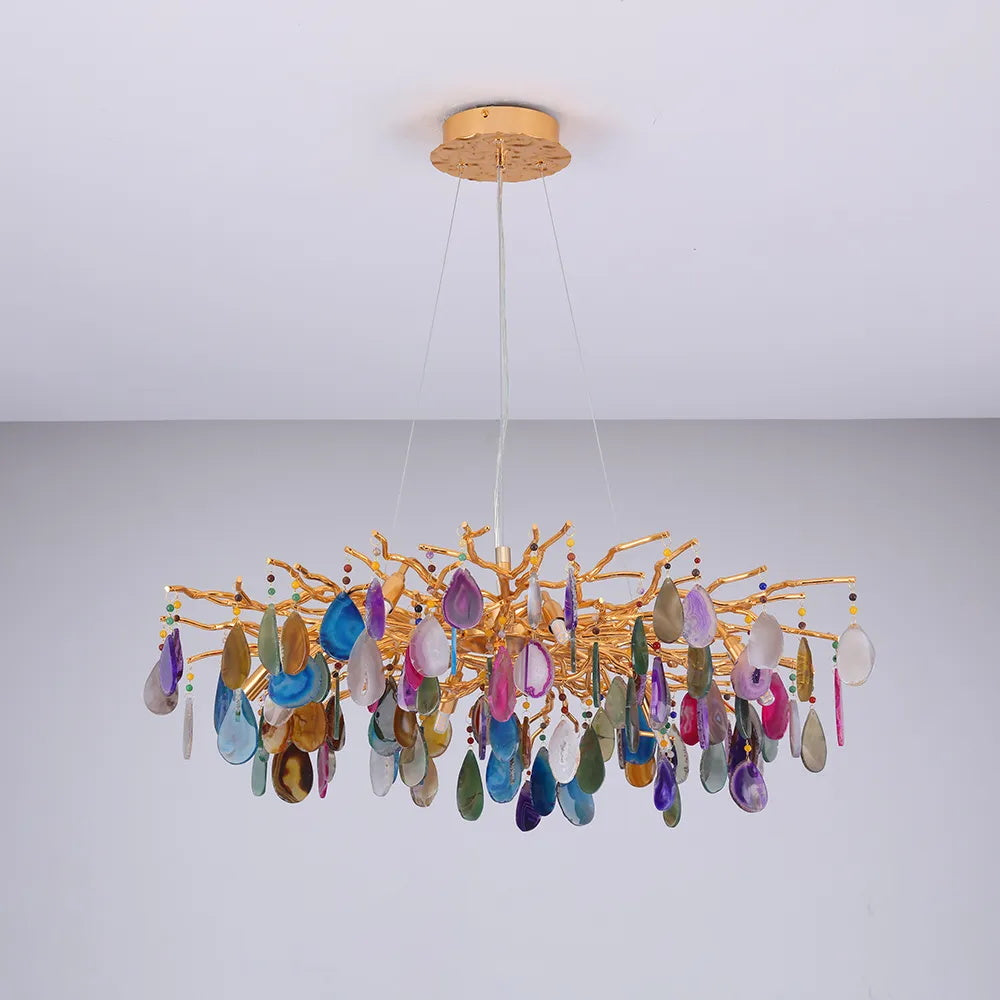 Wide Clérachic chandelier with multicolour agate slices on a gold branch frame, hanging in a pale grey room.