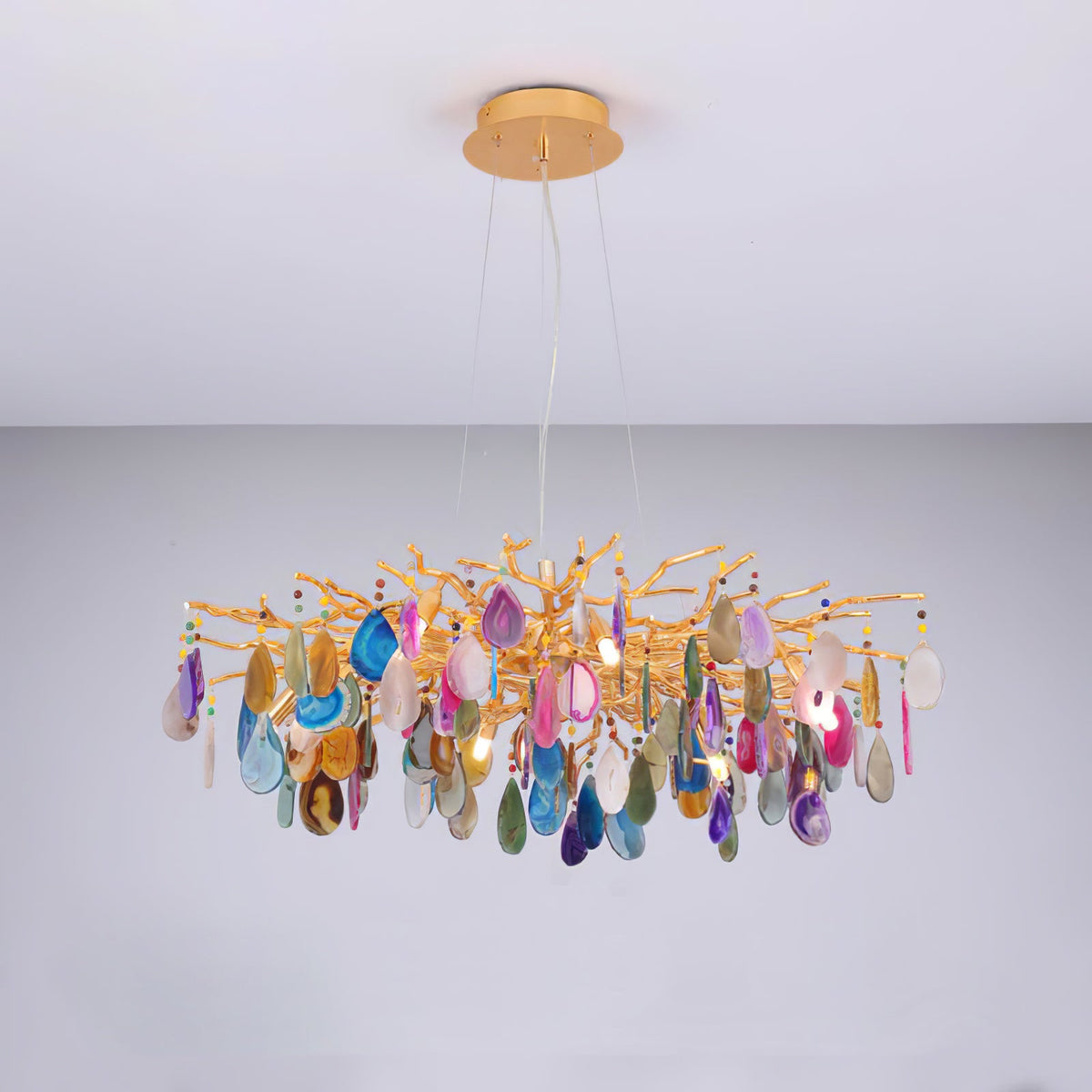 Multicolour agate Clérachic chandelier lit against a pale wall, with pink, blue and amber slices on gold branches.