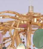 Close view of the gold branch joints and a green agate disc on this Clérachic chandelier, with small coloured beads hanging beside it.