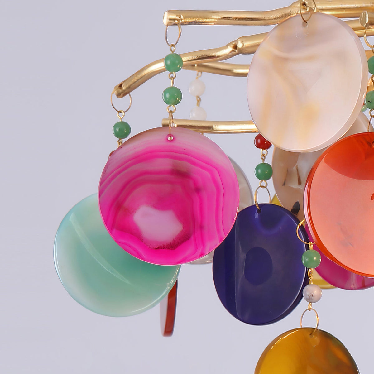 Close view of pink, teal, purple and orange agate discs hanging from gold branches on this Clérachic chandelier.