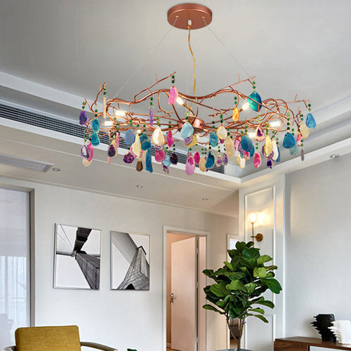 Multicolour Clérachic agate chandelier hanging in a living room with white walls, a large-leaf plant and framed monochrome prints.