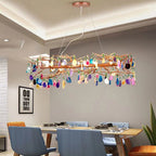 Wide Clérachic agate chandelier above a long dining table with blue chairs, in a room with a recessed ceiling and a framed print.
