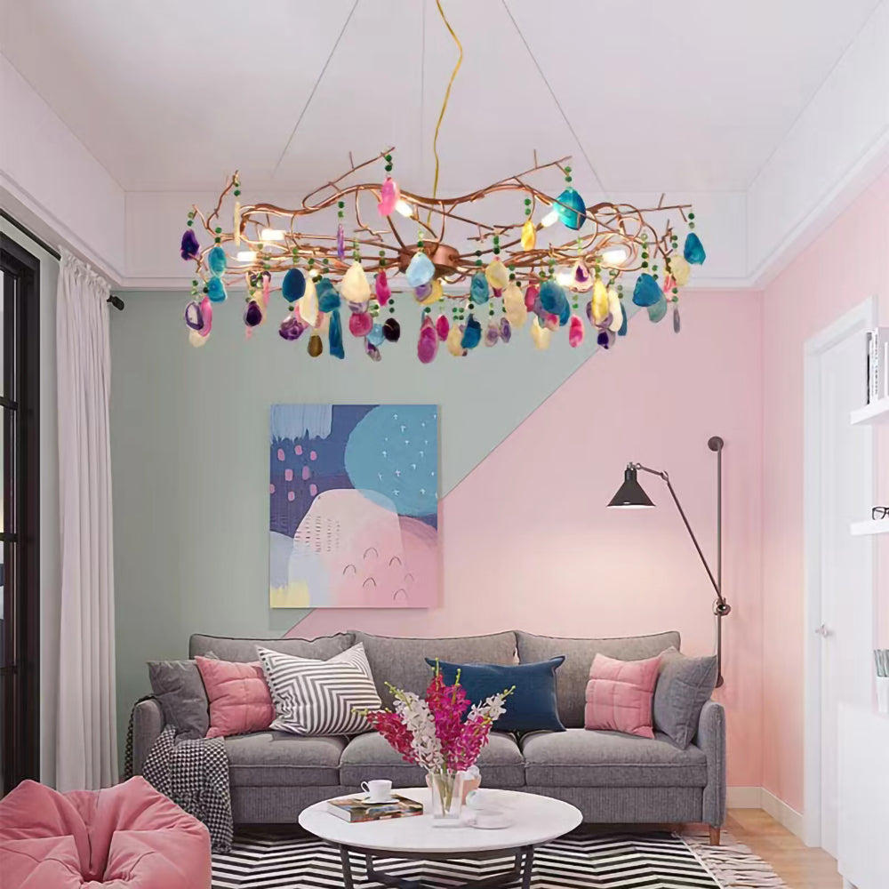 Multicolour Clérachic agate chandelier in a pastel room, above a grey sofa and a round white coffee table with a bunch of flowers.