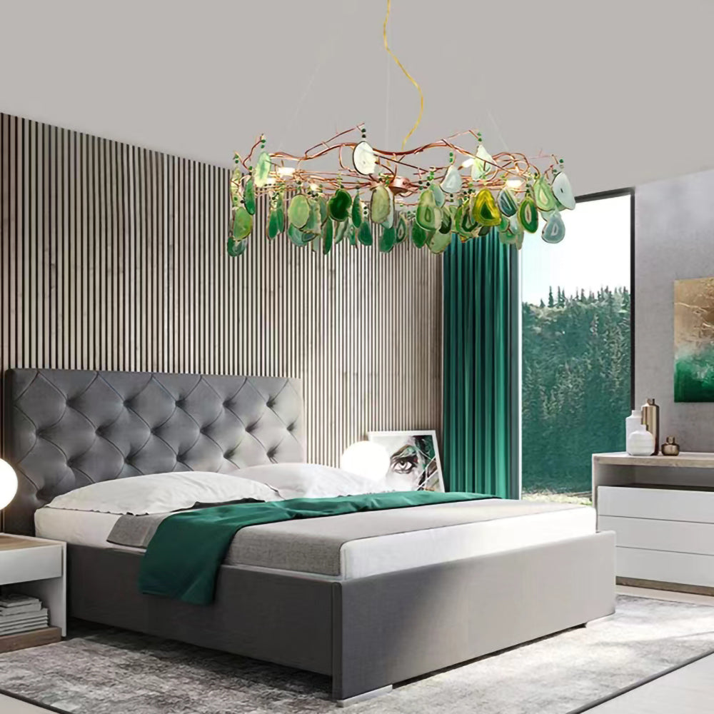 Green-slice Clérachic agate chandelier hanging in a bedroom with a grey tufted bed, a green throw and tall green curtains.