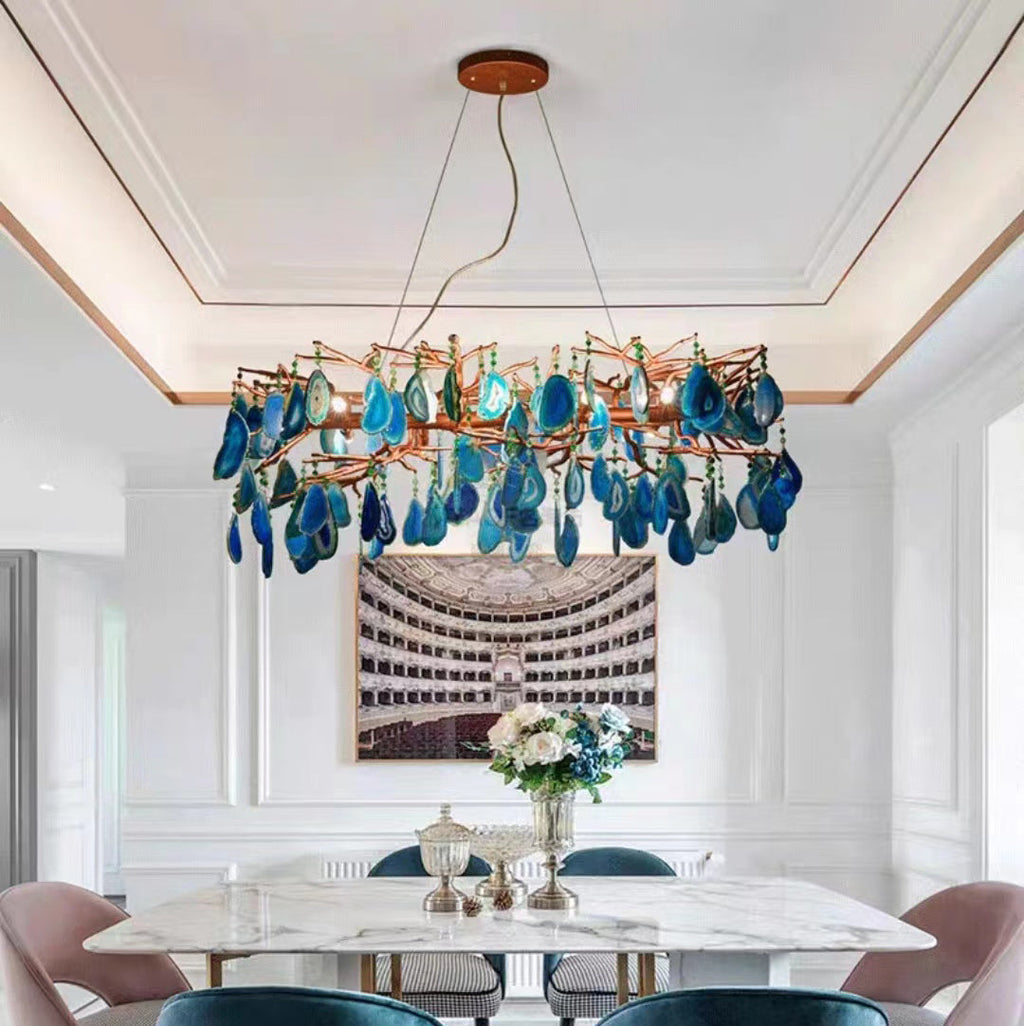 Blue-slice Clérachic agate chandelier above a marble dining table with pink chairs, in a white panelled room under a coffered ceiling.