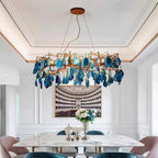 Blue-slice Clérachic agate chandelier above a marble dining table with pink chairs, in a white panelled room under a coffered ceiling.