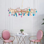 Multicolour Clérachic agate chandelier above a small glass table and two pink chairs, against a white panelled wall.