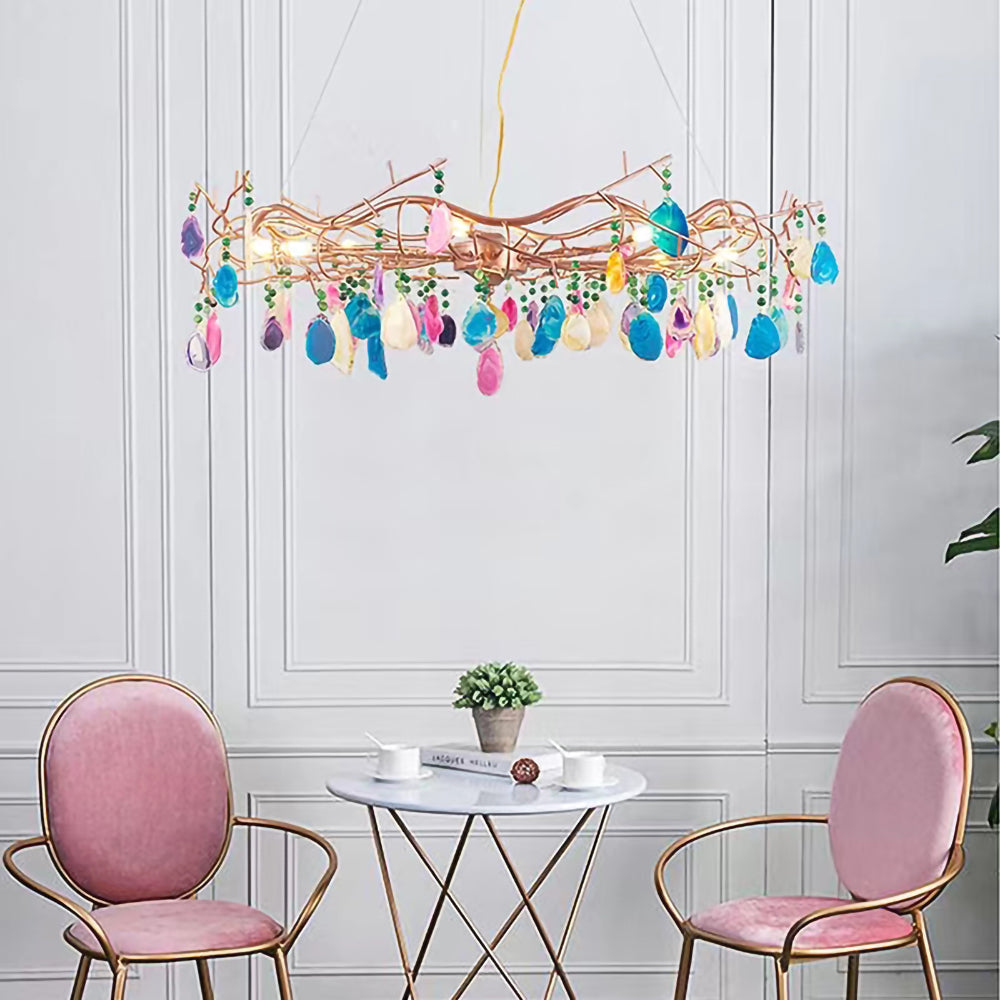 Multicolour Clérachic agate chandelier above a small glass table and two pink chairs, against a white panelled wall.