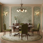 Two green Clérachic agate wall lights on the pale walls of a dining room, with a round table and olive chairs below.