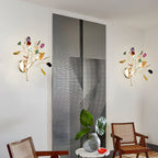 Two multicolour Clérachic agate wall lights on a white wall beside a grey panel, with cane chairs and a plant below.